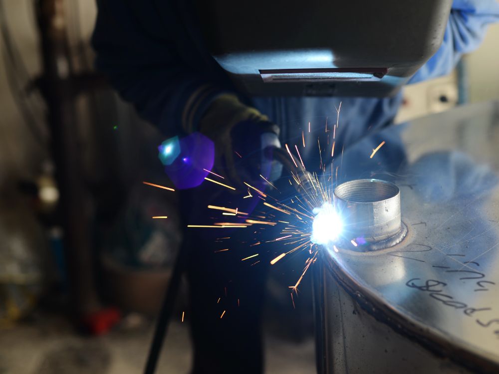 Profissional realizando solda MIG com faíscas visíveis, destacando o uso correto do equipamento e a importância de saber qual melhor arame para solda MIG.