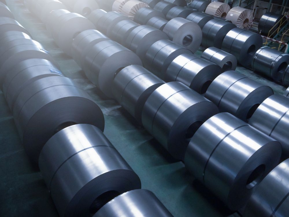 Bobinas de aço em estoque industrial ilustram aplicações práticas para entender qual a diferença entre aços e aços ligas na composição.