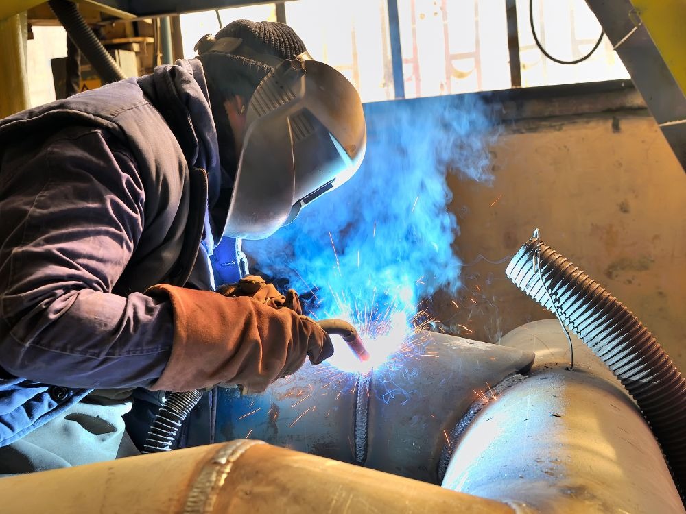 Profissional usando máscara e luvas em processo de soldagem industrial, ilustrando o que é solda MIG