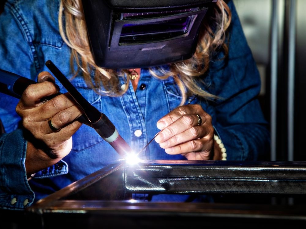 Soldadora realizando acabamento preciso em metal com eletrodo de tungstênio demonstrando visualmente qual a diferença entre a solda MIG e TIG.