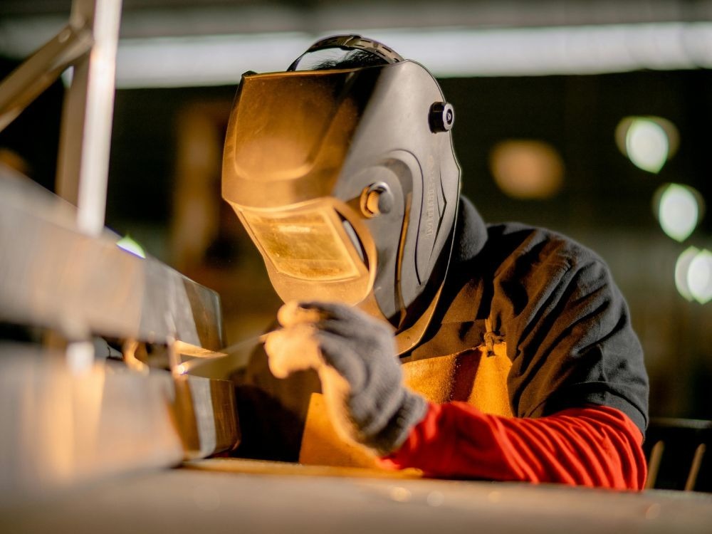 Soldador com máscara de proteção trabalhando em estrutura metálica interna, destacando qualidade e controle obtidos quando a solda MIG é boa.