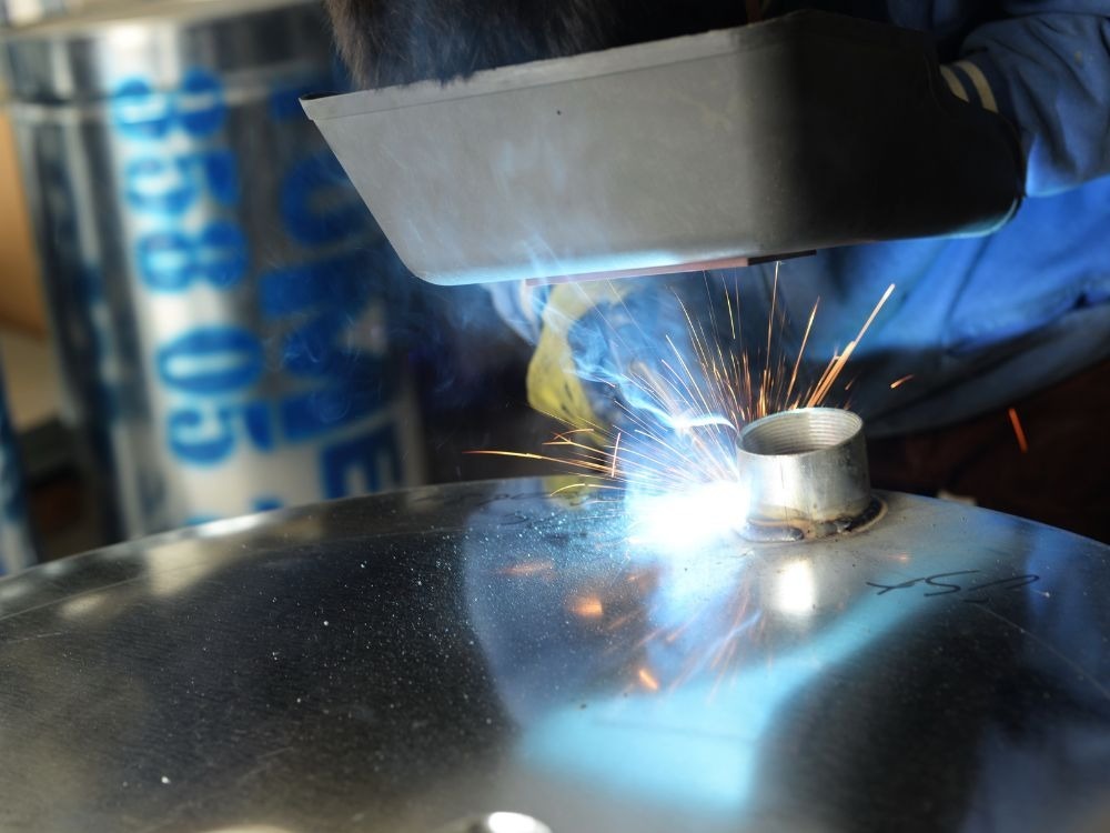 Profissional soldando peça cilíndrica com arco elétrico brilhante, ilustrando estabilidade e acabamento que comprovam que a solda MIG é boa.