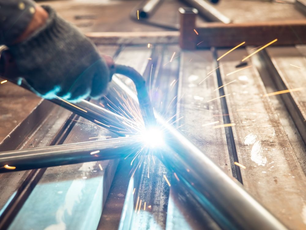 Close da tocha aplicando solda em tubo metálico com grande emissão de faíscas, representando desempenho e precisão quando se analisa se Solda MIG é boa.