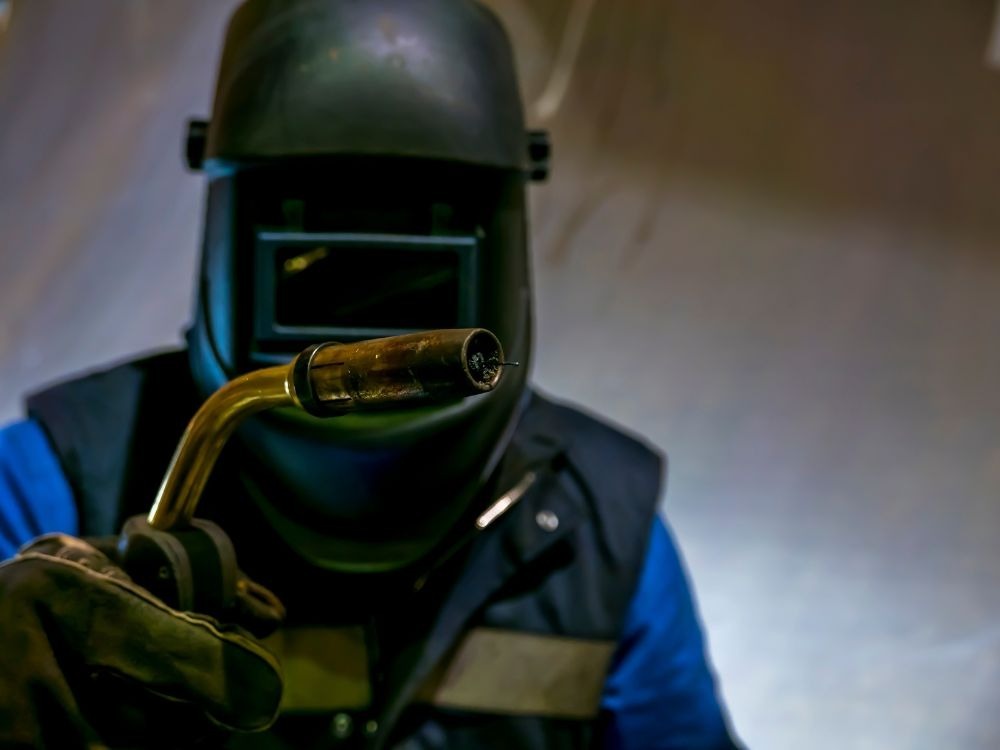 Soldador com máscara de proteção preparando o equipamento para demonstrar a diferença entre solda MIG e MAG em ambiente industrial.