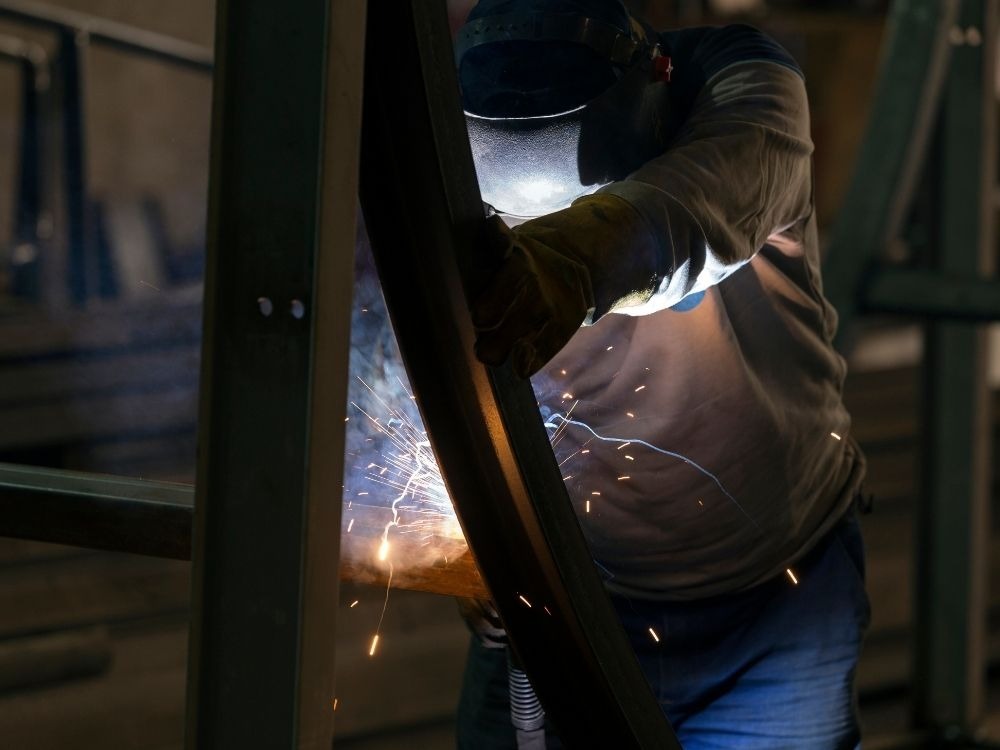 Soldador utilizando equipamento de proteção enquanto realiza união de estruturas metálicas, demonstrando na prática como funciona a solda MAG em ambientes industriais.