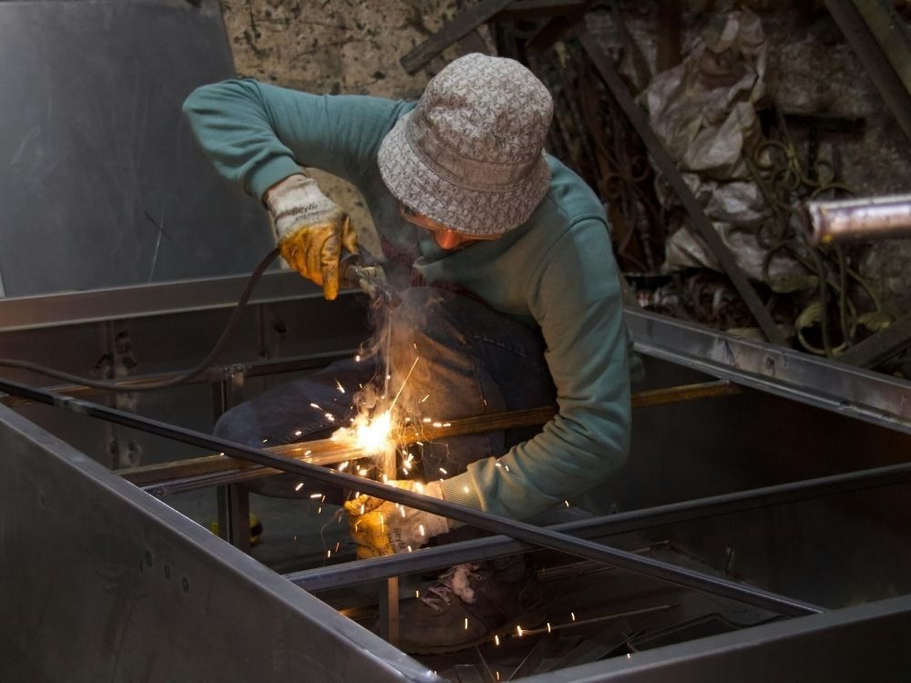 Soldador utilizando equipamento de proteção enquanto realiza união de estruturas metálicas, demonstrando na prática como funciona a solda MAG em ambientes industriais.
