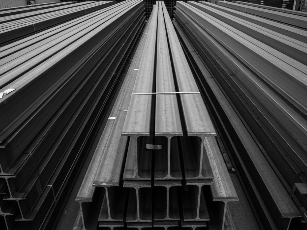 Barras metálicas estruturais empilhadas em estoque industrial, ilustrando O que é viga W? e sua aplicação em estruturas de aço.