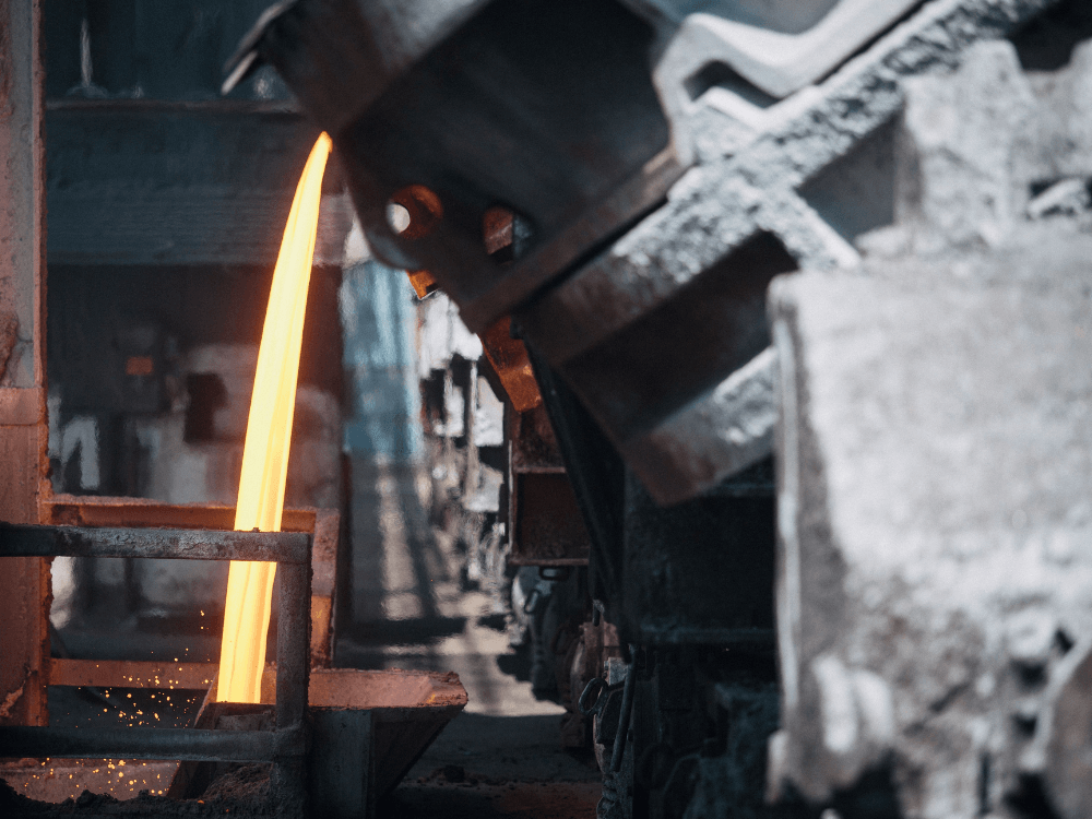 Metal incandescente sendo conduzido por um equipamento industrial durante uma etapa de processamento em uma instalação metalúrgica.